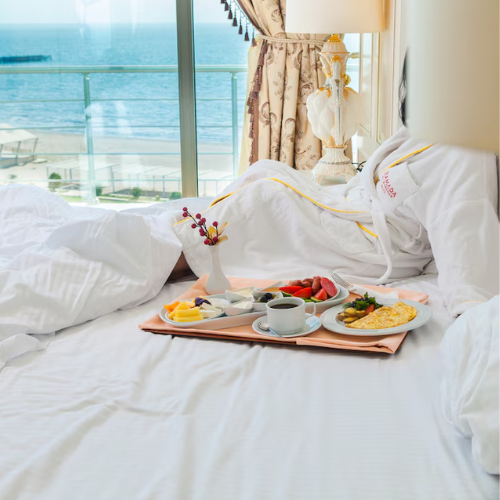 Luxury resort room with ocean view, white bedsheet, and breakfast served on a wooden tray.