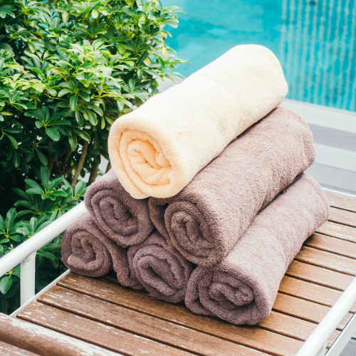 Stacked brown and yellow rolled towels arranged in a pyramid on a wooden poolside table.