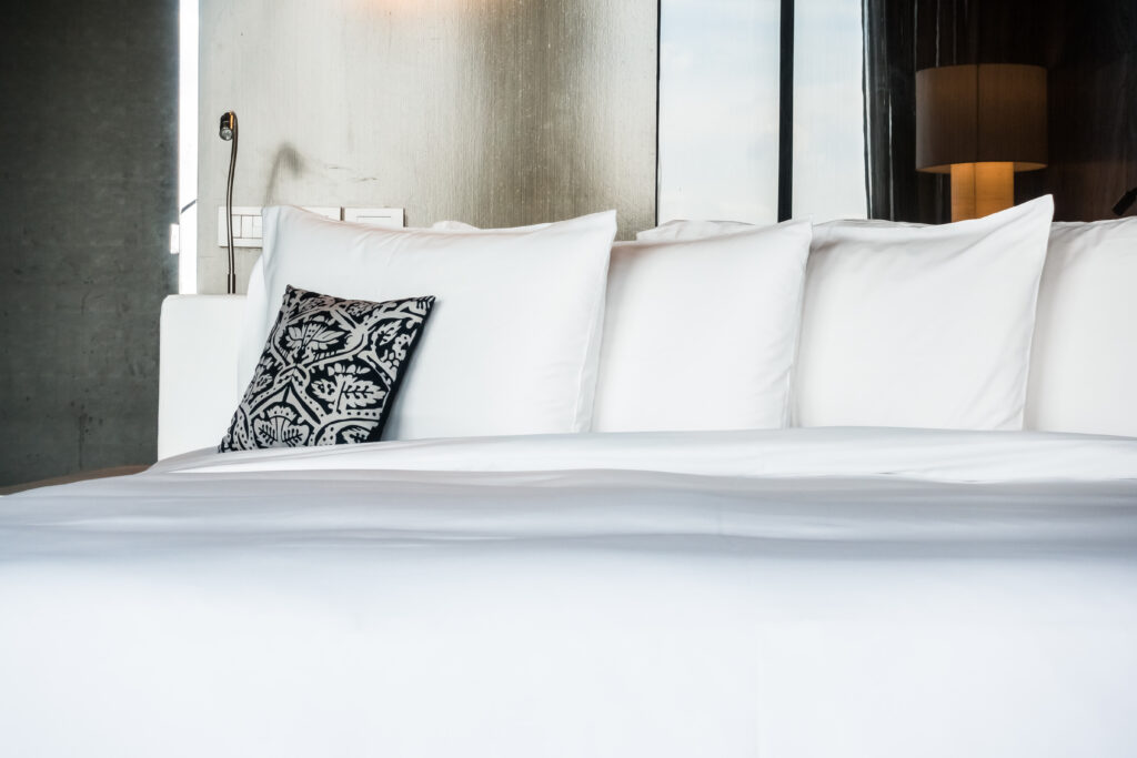 Hotel or resort room with a premium white bedsheet, white pillows, and a single dark gray pillow, neatly arranged on the bed.