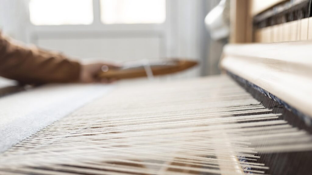 Person operating a weaving machine, creating white fabric threads, showcasing textile craftsmanship.