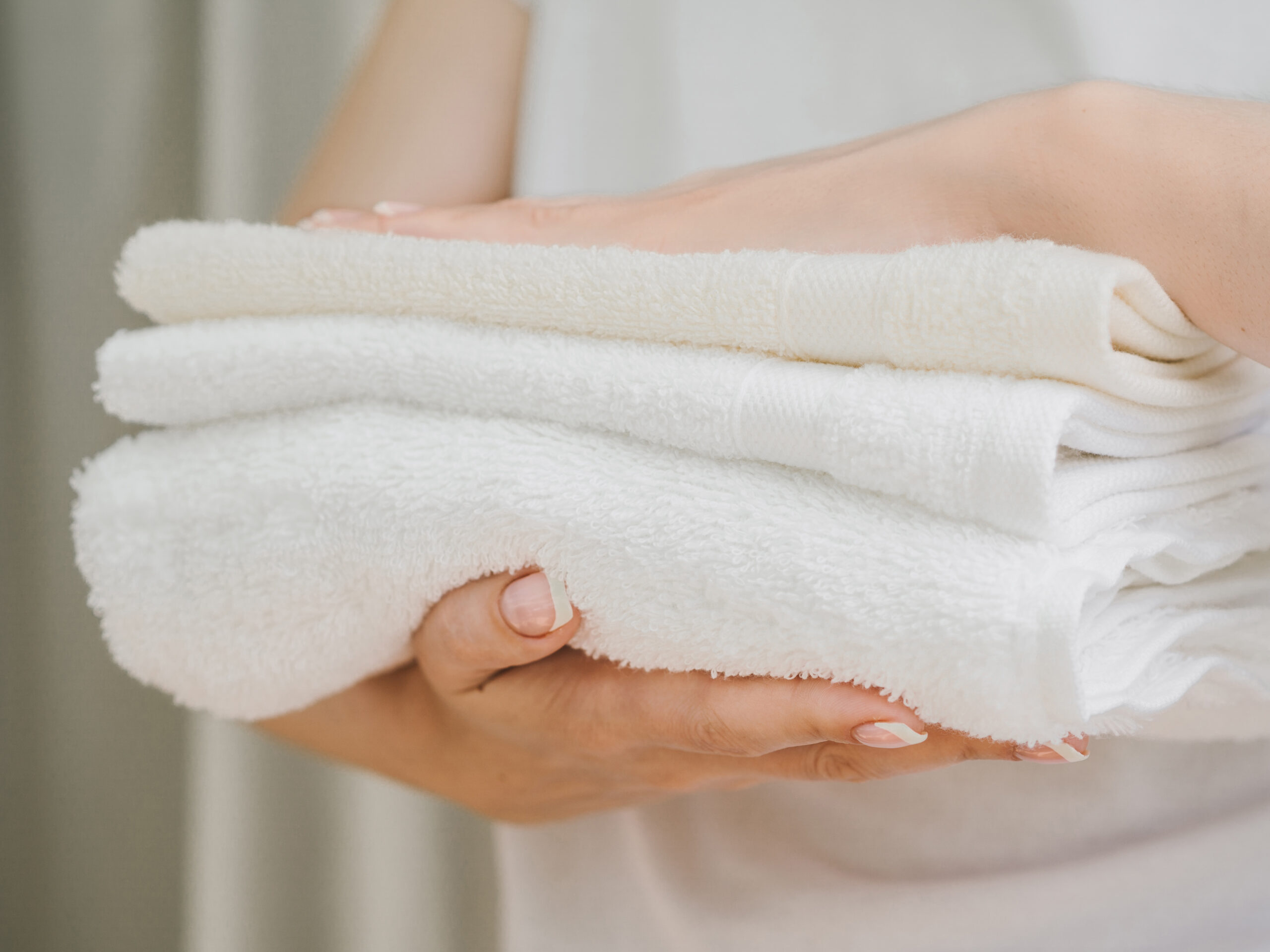Woman holding three neatly folded towels in her hands, smiling and showcasing them.