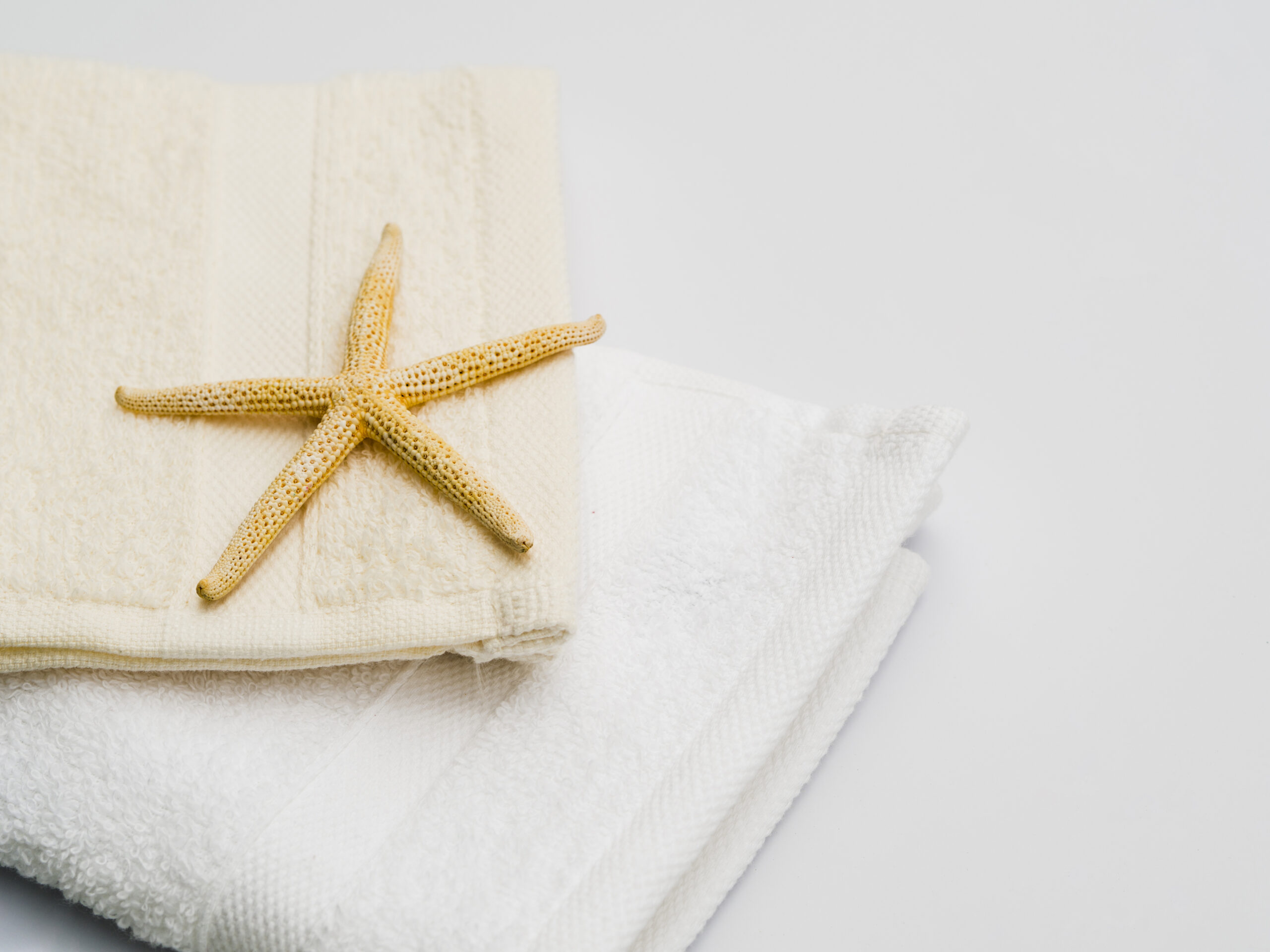 Two folded towels stacked on each other – yellow and white – with a small yellow starfish placed on top.