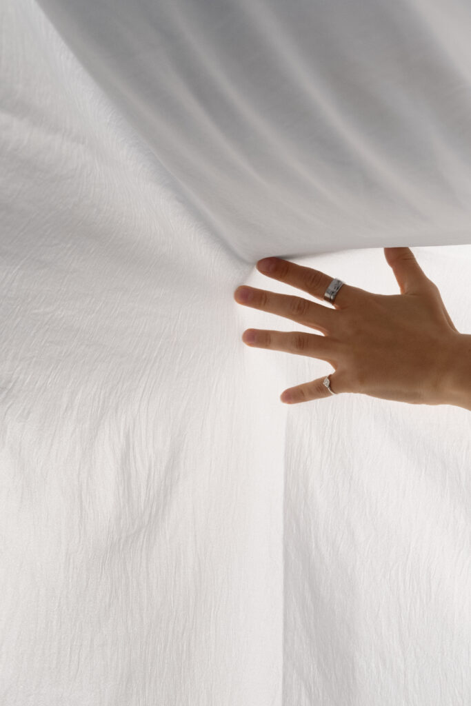 Hand gently feeling a light fabric fluttering in the wind, with sunlight highlighting its texture.