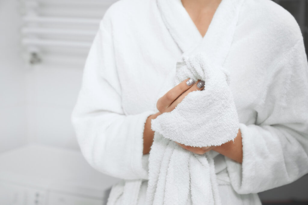 Woman in a white bathrobe holding fresh white towels, symbolizing comfort and luxury.